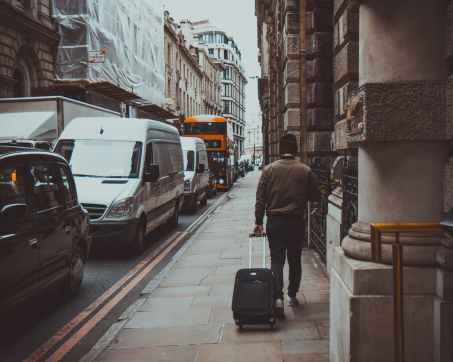 man in brown jacket holding black travel luggage